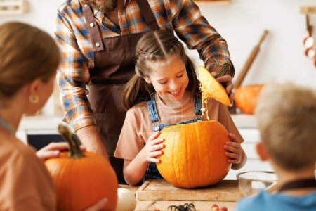 Photo for Happy girl helping dad carve a pumpkin. A cheerful family is preparing for Halloween together by carving a  jack-o-lantern - Royalty Free Image