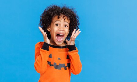 Photo for Happy cheerful african american boy with curly hair in  pumpkin costumes creams in fright while  celebrates Halloween on  bright blue background - Royalty Free Image