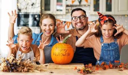 Foto de Feliz familia madre, padre y dos hijos hace un gesto de miedo con calabaza durante la celebración, preparando decoraciones de Halloween en casa - Imagen libre de derechos