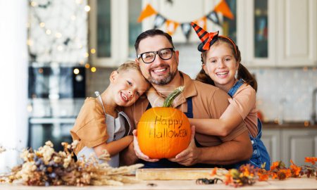 Foto de Feliz familia de niños abrazando padre con calabaza con inscripción Feliz Halloween durante la celebración, preparando decoraciones de Halloween en casa - Imagen libre de derechos