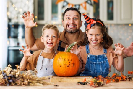 Téléchargez les photos : Heureux enfants de la famille et le père souriant à la caméra et geste effrayant avec citrouille pendant la célébration, la préparation des décorations d'Halloween à la maison - en image libre de droit