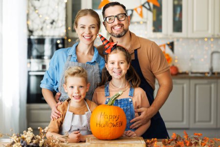 Téléchargez les photos : Bonne famille mère, père et deux enfants souriant à la caméra avec citrouille pendant la célébration, préparer des décorations d'Halloween à la maison - en image libre de droit