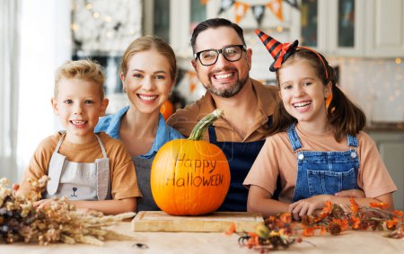 Téléchargez les photos : Bonne famille mère, père et deux enfants souriant à la caméra avec citrouille pendant la célébration, préparer des décorations d'Halloween à la maison - en image libre de droit
