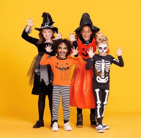 Foto de ¡Feliz Halloween! Niños alegres en trajes de carnaval y maquillaje hacen un gesto terrible sobre fondo amarillo brillante - Imagen libre de derechos