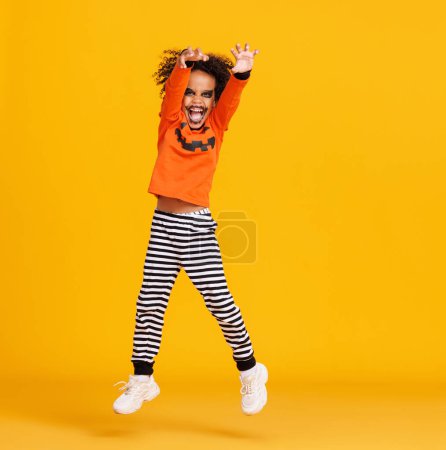 Foto de Feliz niño alegre en traje de calabaza saltando y celebra Halloween y se ríe en el fondo amarillo - Imagen libre de derechos
