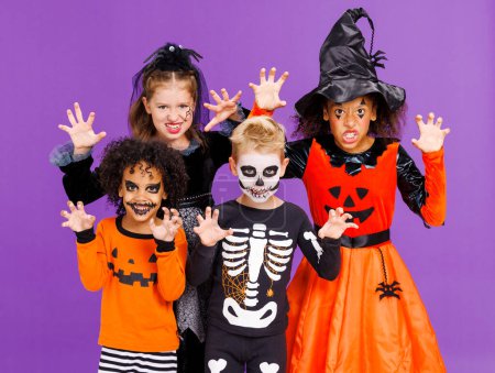 Téléchargez les photos : Joyeux Halloween ! Enfants gais en costumes de carnaval et maquillage faire un geste terrible sur fond violet lumineux - en image libre de droit