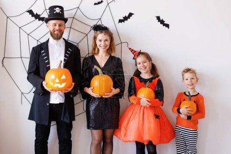 Photo for Cheerful family mother father and children in carnival costumes celebrate Halloween near gray wall with cobwebs and bats - Royalty Free Image