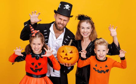 Téléchargez les photos : Mère de famille joyeuse père et les enfants en costumes de carnaval fait geste effrayant célébrer Halloween sur fond jaune coloré - en image libre de droit