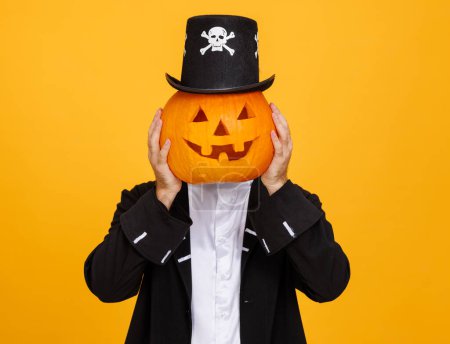 Téléchargez les photos : Homme heureux dans un costume squelette couvre la tête avec de la citrouille et célèbre Halloween et rit sur fond jaune - en image libre de droit