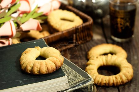 Photo for Traditional festive Algerian Kaak dry cookies ring named " kaak of tlemcen in arabic " tlemcen is a town in algeria in basket above book with tea cup - Royalty Free Image