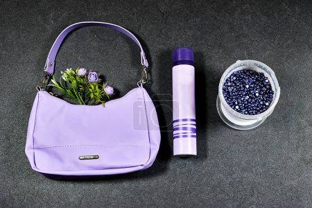 Foto de Stylish, fashion purple handbag with flowers and deodorant bottle with  seed wax on gray grunge background - Imagen libre de derechos