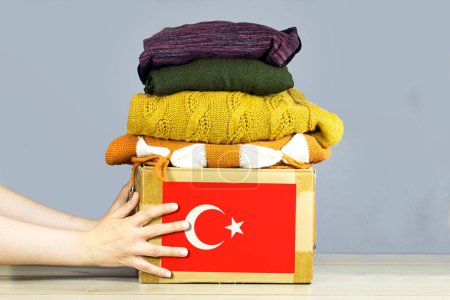 closeup woman hands holding carton box with used clothes for donation and turkey flag Earthquake, catastrophe volunteering