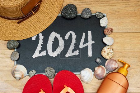 concepto de verano, crema solar y zapatilla con 2024 en pizarra y piedras. concha de mar sobre mesa de madera