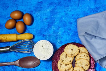 Photo for Homemade cookies in  plate with eggs and wire whisk and eggs, flour  on blue grunge background - Royalty Free Image