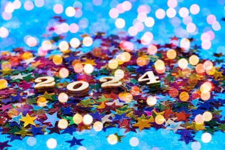 Ein frohes neues Jahr 2024 mit Holzzahlen auf bunten Sternen Konfetti mit leichtem Bokeh