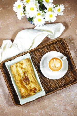 Photo for Homemade puffed pastry apple tart in esparto halfah basket with daisy flowers and latte art coffee cup - Royalty Free Image