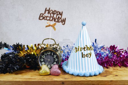 Photo for Birthday boy party concept, heart glitters toy and blue hat with alarm clock and happy birthday test and colorful tinsel on wood table - Royalty Free Image