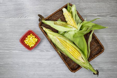 Photo for Fresh corn cob in esparto halfah basket and bowl on wood table - Royalty Free Image