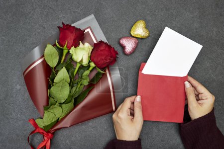 Foto de Hermosas flores de ramo de rosas con la mano sosteniendo un sobre con feliz día de San Valentín - Imagen libre de derechos