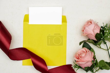 Photo for Blank greeting card, flyer or invitation card mockup with pink roses, red ribbon on grunge background - Royalty Free Image