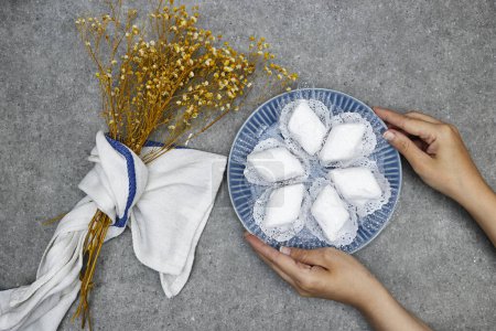 hands holding plate with algerian traditional cookies named makrout is a almond paste forming diamond shape and covered with icing sugar and gypsophila flowers