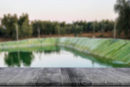 empty rustic wooden table for mockup product display near a view of plastic water retention basin for irrigation in agriculture
