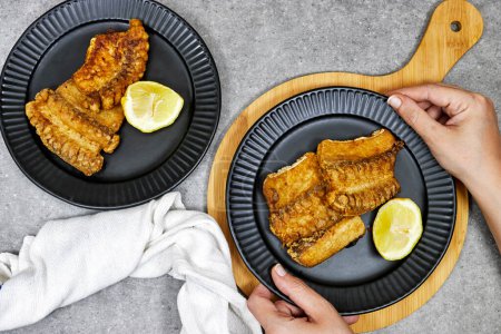 hands holding a plate of grilled Ray or skate filet decorated with slice of lemon