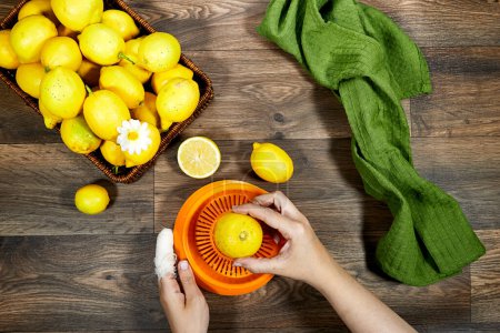 Female hand squeezes fresh lemon juice on orange plastic squeezer on wood table