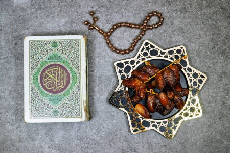 geschlossenes muslimisches Buch mit arabischer Kalligraphie Koran-Übersetzung: Heiliges Buch der Muslime und Dattelfrucht, Tasbih. Iftar-Ramadan-Konzept