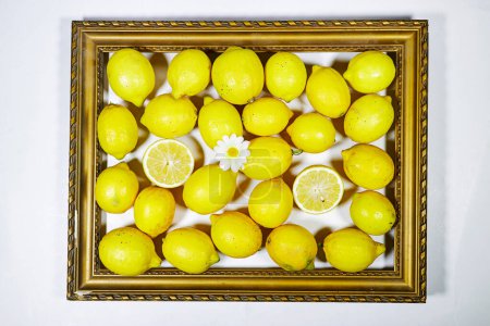 Lifestyle-Foto von frischer Zitrone mit Gänseblümchen auf vergoldetem Bilderrahmen