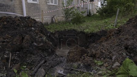 Dug dirty pit in ront of the house with grass behind. Clip. Repair works of city communications