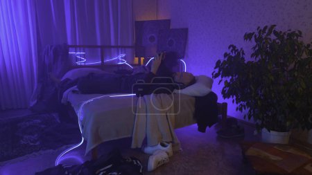 Photo for Stressed man lie on the bed at home while holding his head neon background. High quality photo - Royalty Free Image