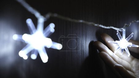 Close-up of womans hand touching the beautiful electric Christmas garland of bright lights hanging on the wooden wardrobe or door. Christmas mood