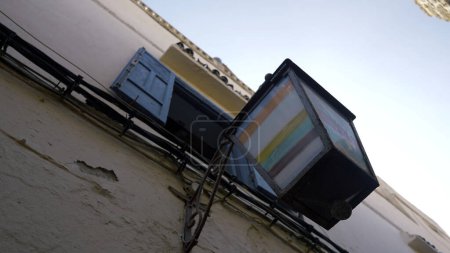 Bottom view of a house wall with hanging street lamp. Action. Colorful street lamp and blue wooden shutters