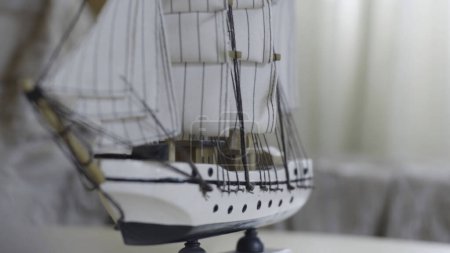 Nahaufnahme des kleinen weißen Schiffsmodells aus Holz auf gestreiftem Hintergrund auf dem unscharfen hellen Hintergrund. Hobby und Sammlungskonzept