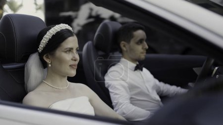 Novia y novio en ropa de boda sentado en coche cabriolet. Acción. Hombre y mujer en coche de lujo