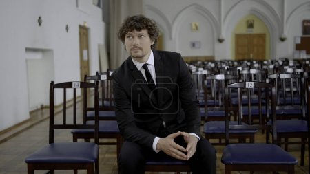 Photo for Young man with curly hair in black and white classic suit in empty church. Action. Groom prepared for his wedding - Royalty Free Image