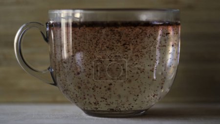 Hibiskustee mit kochendem Wasser in einer großen Glasschale auf hölzernem Wandhintergrund zubereiten. Großaufnahme von rotem Früchtetee in einem transparenten Glasbecher, der auf einer flachen Tischfläche steht.