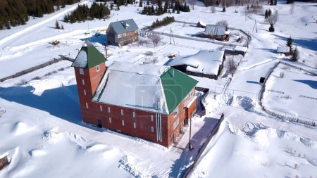 Luftaufnahme des Dorfes im Winter, Details aus der Landschaft. Clip. Rotes Backsteinhaus und kleinere Häuser, schneebedeckter Boden