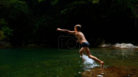 Zeitlupe eines Jungen, der in einen Wasserfall und einen natürlichen Teich springt. Kreativ. Junge Kind hat Spaß im Dschungel
