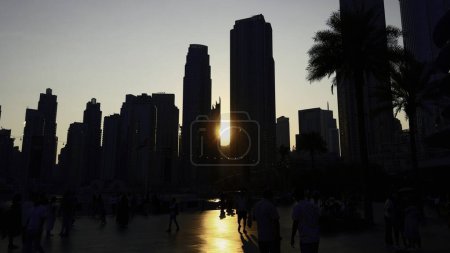 Foto de Puesta de sol entre las torres de rascacielos y caminar multitud irreconocible de personas. Acción. Distrito central de Dubai ciudad - Imagen libre de derechos