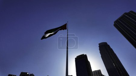 Low angle view of a waving flag against blue sky. Action. Dubai, UAE, architecture and waving flag