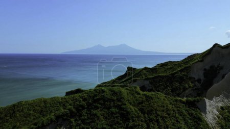 Breathtaking aerial view of dramatic green mountains and blue ocean. Clip. Beautiful nature background of green jungle mountain peaks revealing turquoise water surface