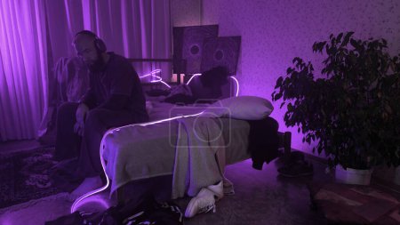 Depressiver Mann sitzt mit Kopfhörern auf seinem Bett. Medien. Junger Mann verspürt Angst