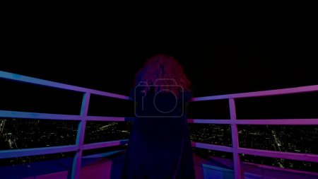 Femme sur le toit d'un immeuble. Les médias. Sorcière moderne sur le toit d'un gratte-ciel la nuit. Vue arrière d'une femme sur le toit d'un gratte-ciel la nuit.