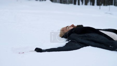Glücklicher junger Mann im märchenhaften Winterwald auf Schnee liegend. Medien. Konzept der Religion und Gefühl der Einheit mit der Natur