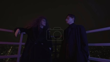 Low angle view of a couple standing on roof and looking at each other. Media. Man and woman with wild beautiful curly hair at night