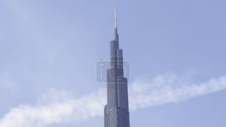 Low angle view of Burj Khalifa with blue sky behind. Action. Modern glass facade skyscraper in the city center