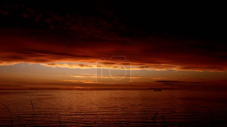 Fairytale breathtaking sunset above rippling river with a floating boat. Clip. Dark red and orange sky, heavy clouds above water