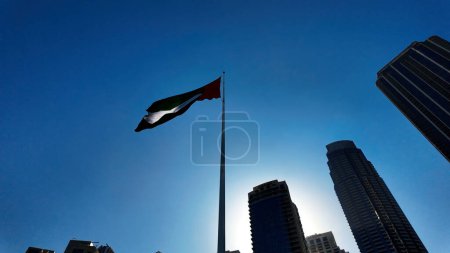 Low angle view of a waving flag against blue sky. Action. Dubai, UAE, architecture and waving flag
